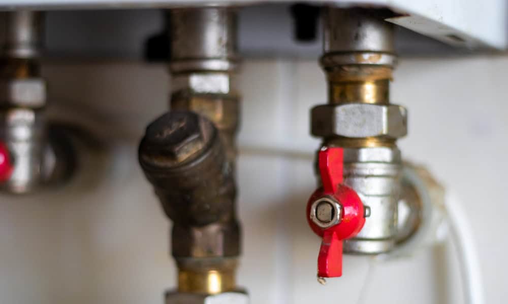 Close-up of metal water heater valves with a prominent red shut-off lever.