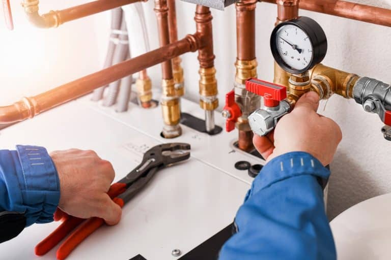 Technician adjusting pressure valve on a modern heating system with copper piping.