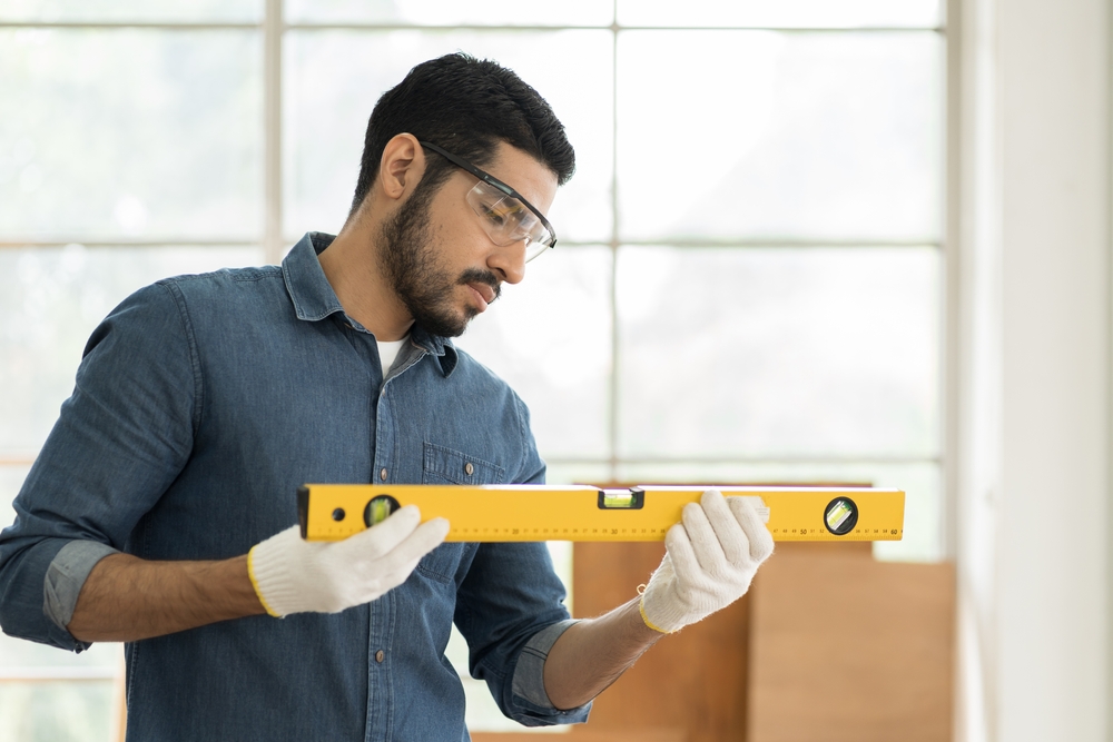 A carpenter carefully levels a surface with a spirit level in a bright workshop.