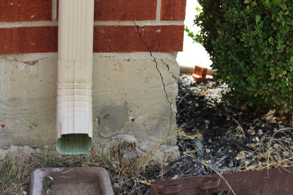 Foundation trouble—visible cracks near the downspout signal potential water damage and structural issues.