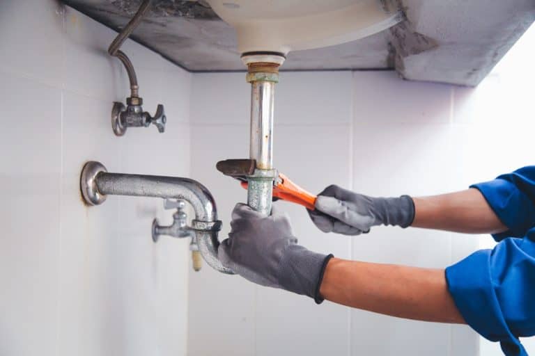 Plumber at work fixing a leaky pipe under a sink with a wrench.