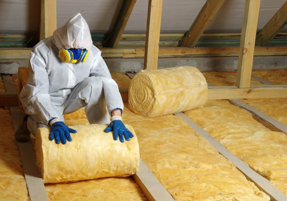 Installing fiberglass insulation in the attic for a warmer, energy-efficient home.