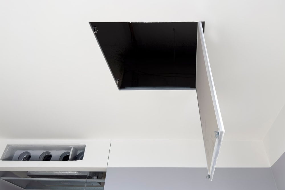 Ceiling access panel open, revealing a dark attic space above modern interior ductwork.