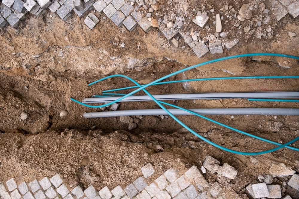 Underground utility installation with fiber optic and conduit pipes beneath cobblestone pavement.