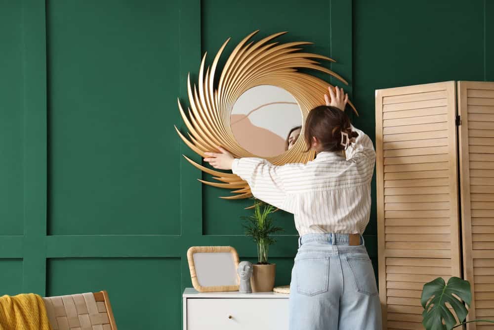 Hanging a stylish sunburst mirror in a vibrant green room, adding a touch of elegance and personality to the space.