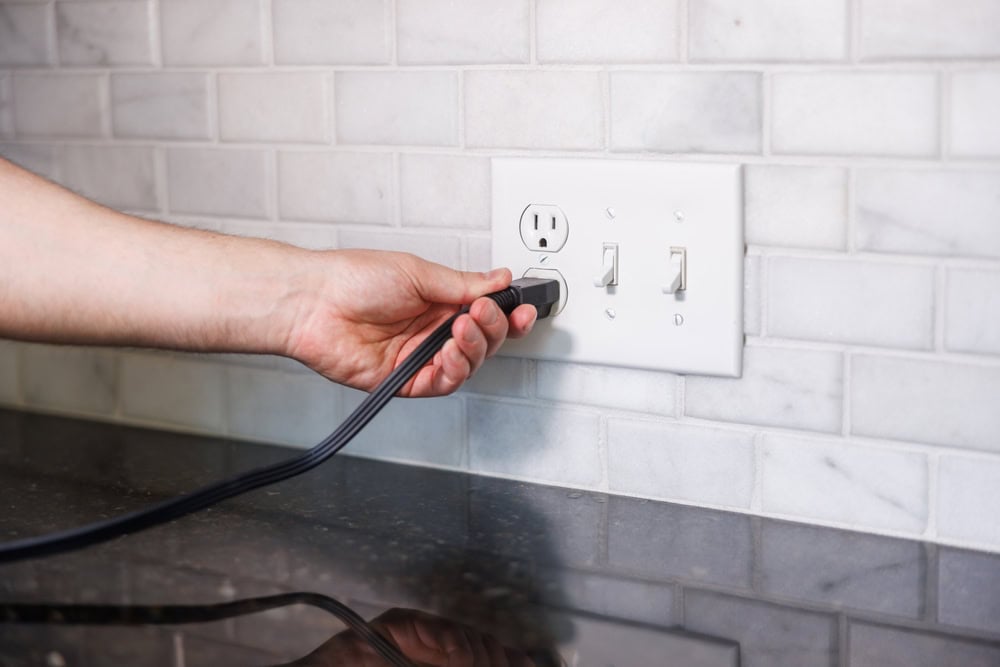 Powering up: A hand plugs an appliance into a kitchen outlet.
