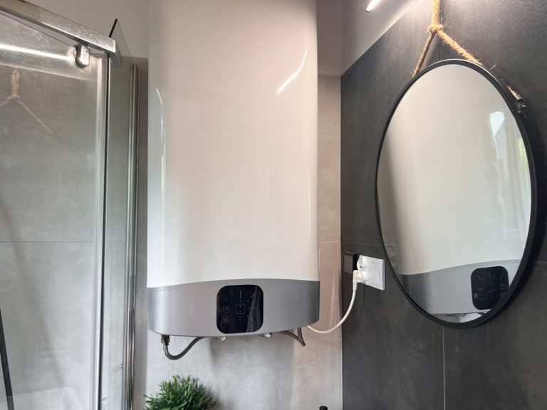 Modern bathroom with a sleek water heater, round mirror, and stylish shower enclosure.