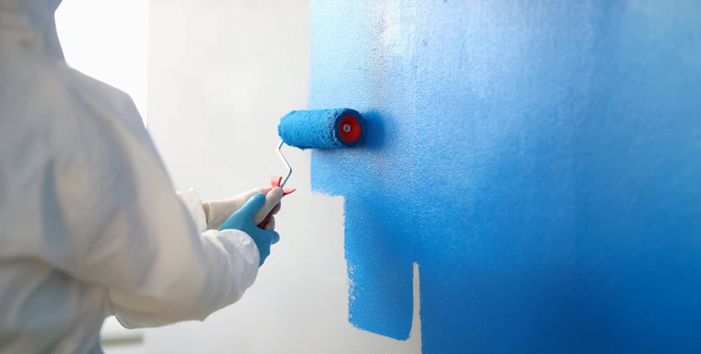 A painter meticulously applies a vibrant blue coat to the wall, bringing color to life.