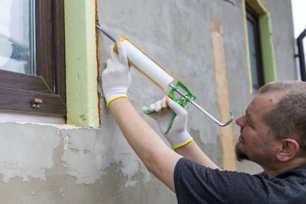 Construction worker applies caulking around a window frame while wearing protective gloves during a home renovation project.