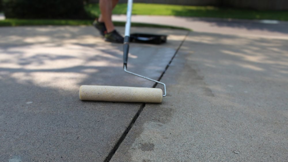 Sealing the driveway crack with a paint roller.