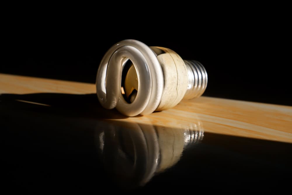 A compact fluorescent light bulb lies in dramatic lighting, casting a soft reflection on a glossy surface.