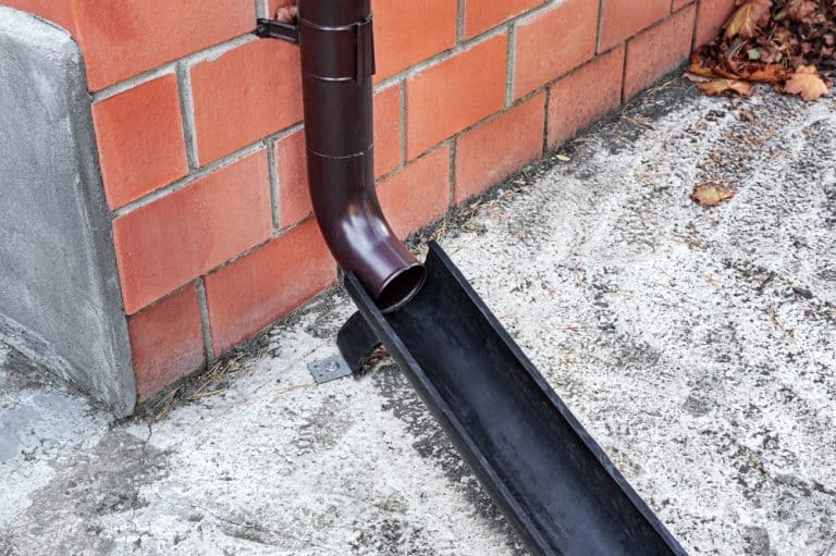 Efficient rainwater drainage—downspout directing flow against a red brick wall.