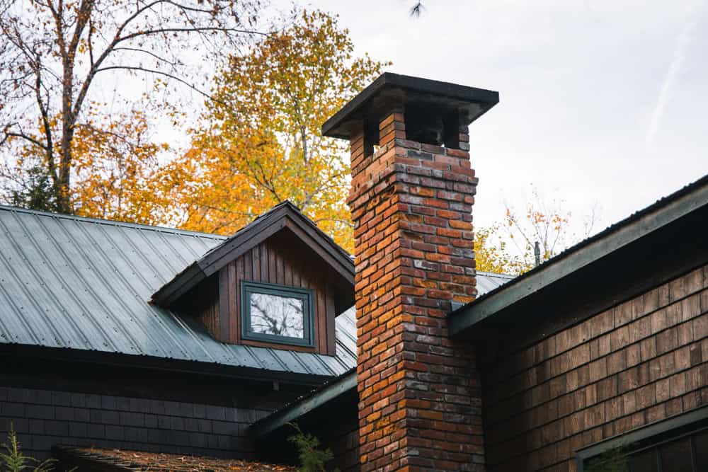 A cozy cabin chimney rises against a backdrop of golden autumn foliage.