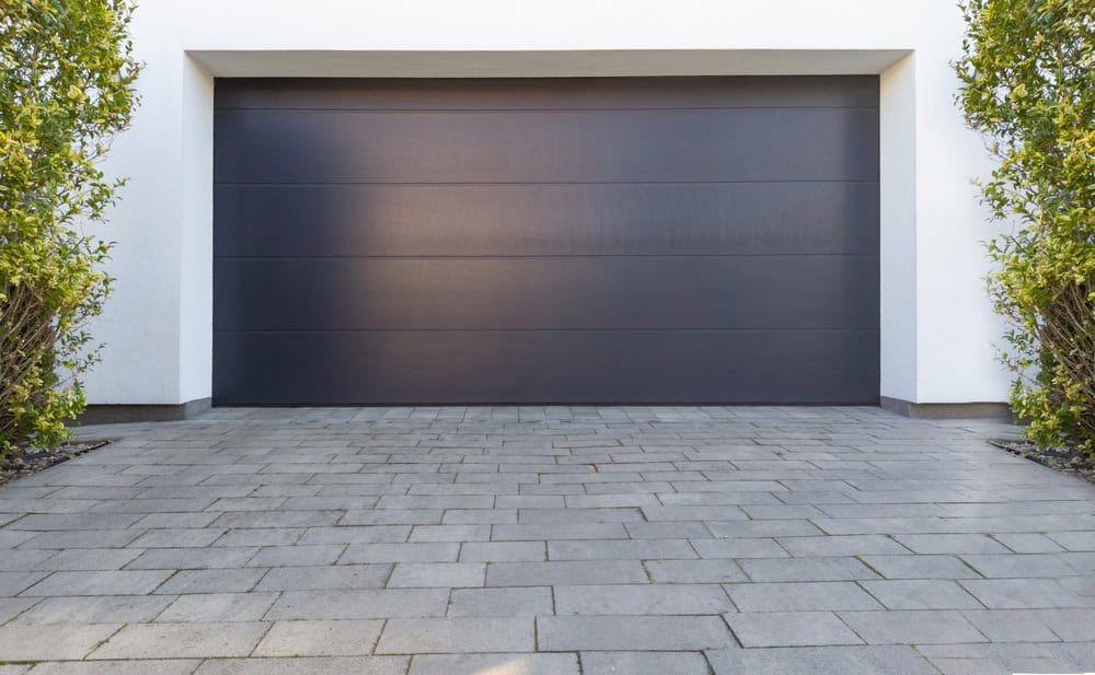Modern elegance: a sleek black garage door framed by lush greenery on a stylish stone driveway.