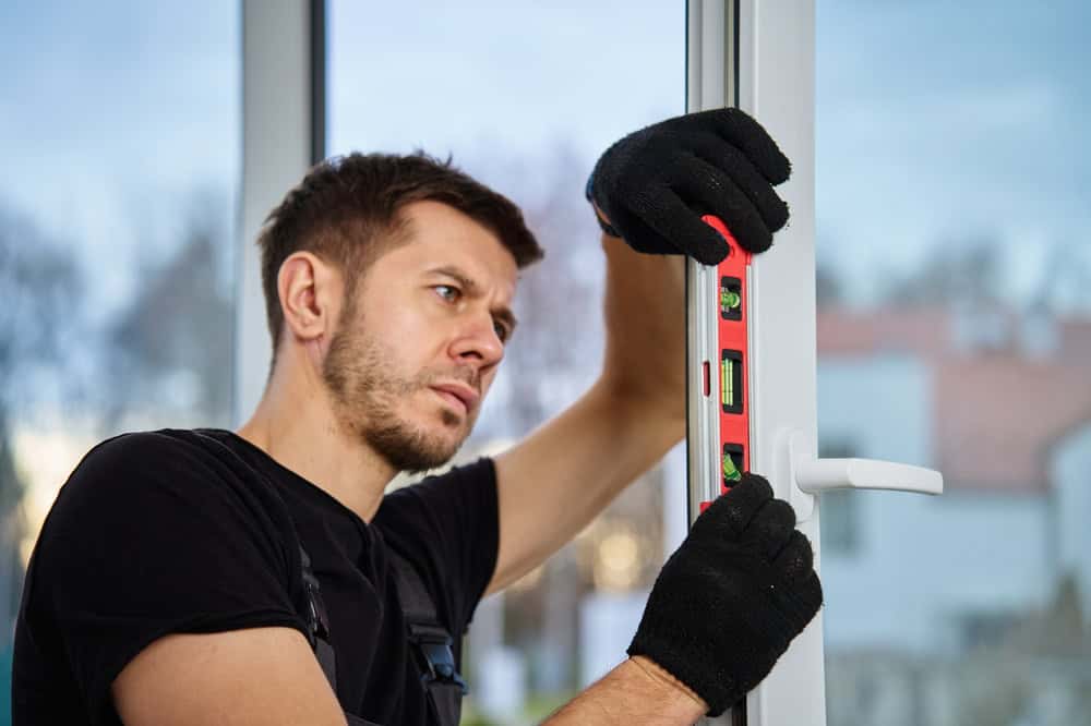 A handyman carefully adjusts a door frame, using a spirit level to ensure precision.