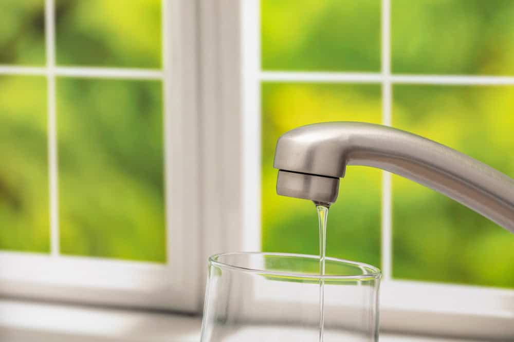Fresh tap water pours into a glass by a sunlit kitchen window, reflecting purity and simplicity.