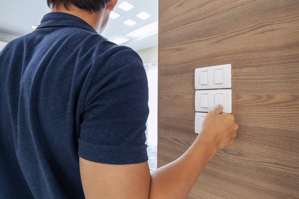 A person reaching to flip a light switch in a modern wooden-paneled room.