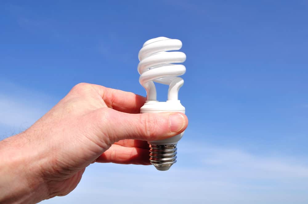 A hand holds a compact fluorescent light bulb against a clear blue sky