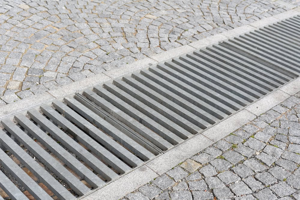 Modern metal drainage grate set into a cobblestone pavement, blending function with urban design.