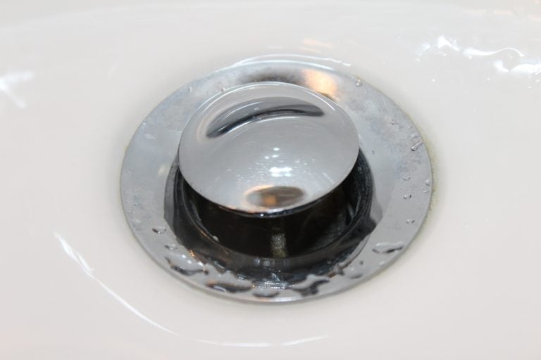 Close-up of a shiny chrome sink drain stopper with water droplets.