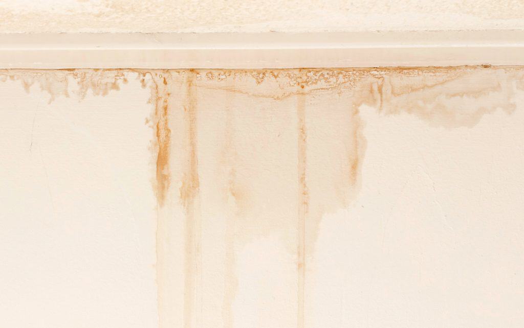 Water damage trails on an off-white wall, creating rust-colored stains that streak downward from the ceiling