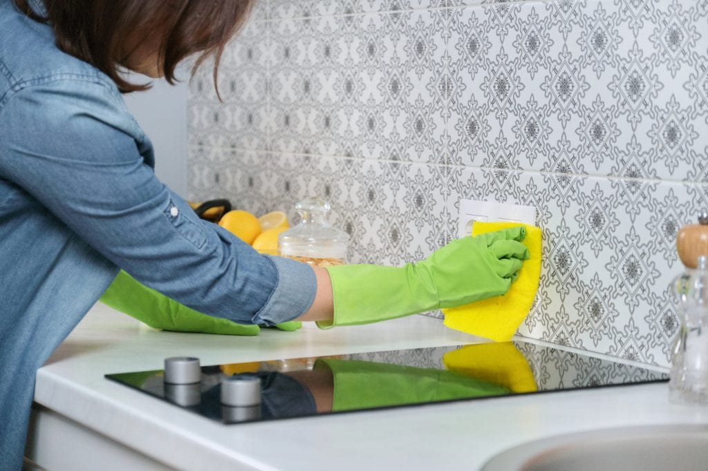 Cleaning the kitchen tiles with a bright yellow sponge and green gloves.