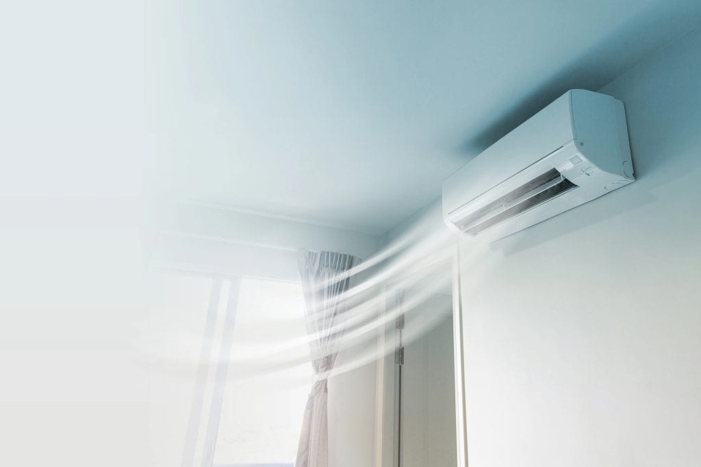 Cool air streams elegantly from a wall-mounted air conditioner, creating visible currents that dance with the light sheer curtains in a minimalist white room.