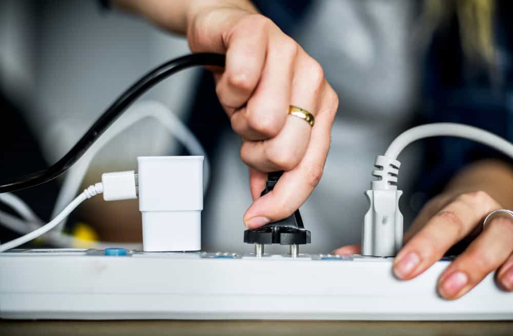 A close-up of hands connecting a device to a surge protector.