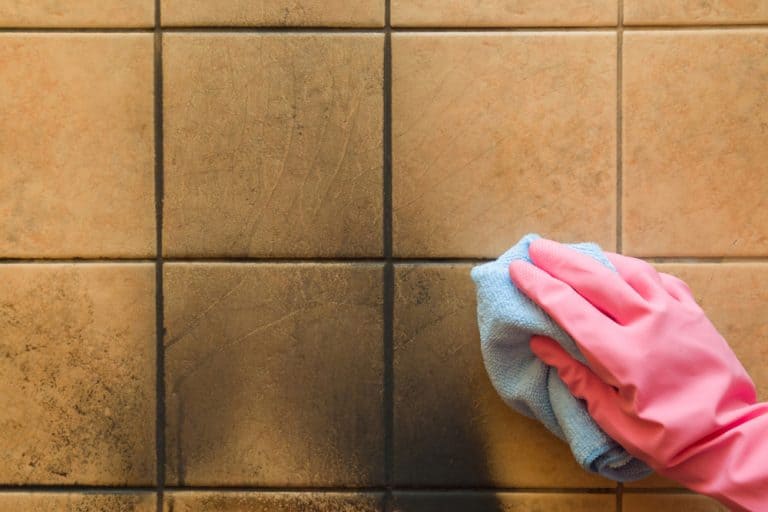 Cleaning stubborn soot stains off kitchen tiles with a blue cloth and pink gloves.