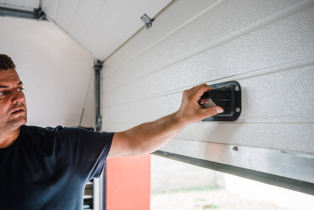 Man opens a white garage door using the interior emergency release handle.