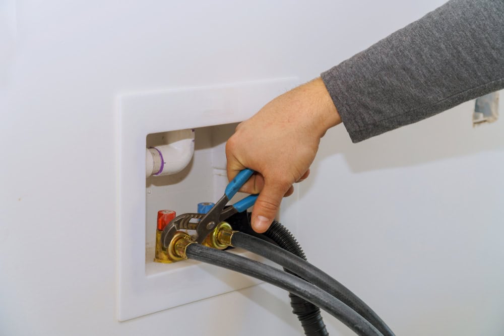 Tightening washer hose connections during laundry room installation.