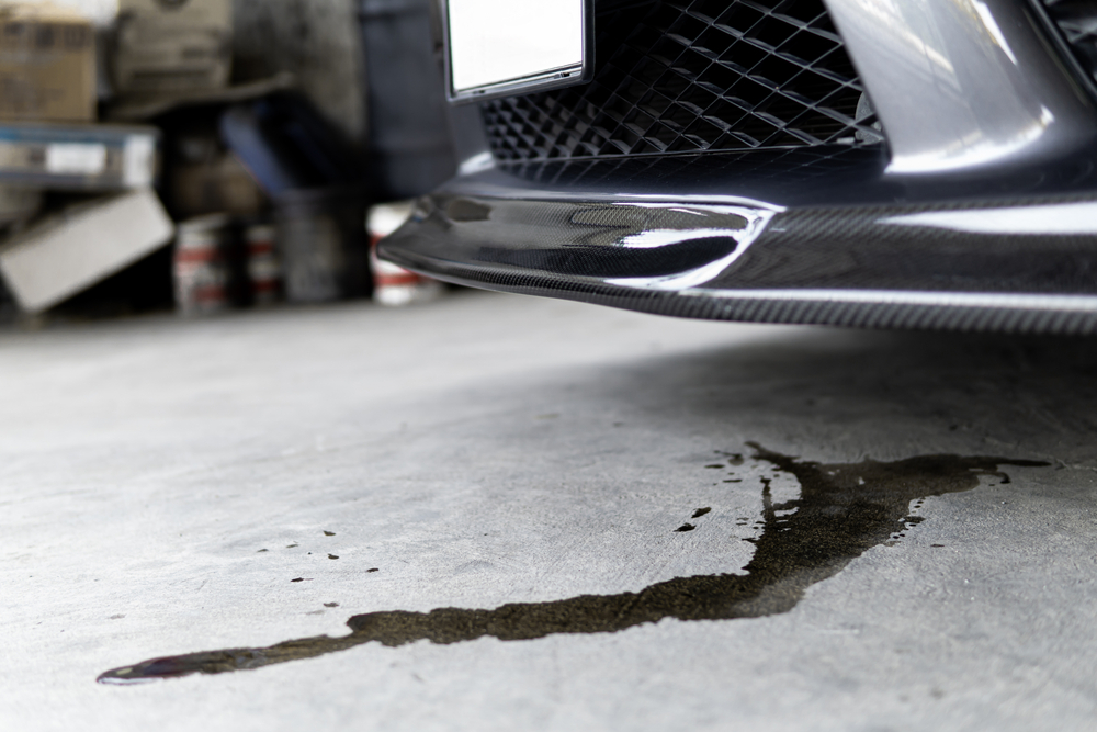 Oil leak on a garage floor beneath a luxury vehicle's carbon fiber front splitter