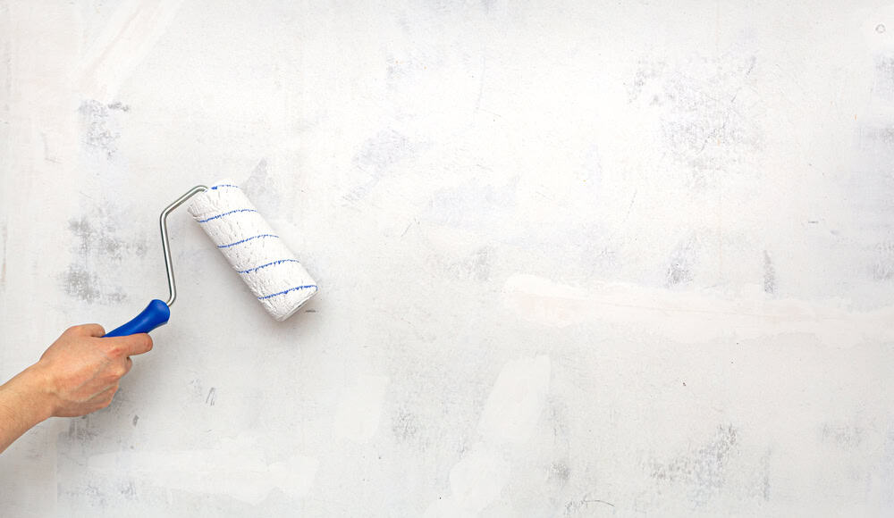 A hand holding a paint roller against a partially painted wall