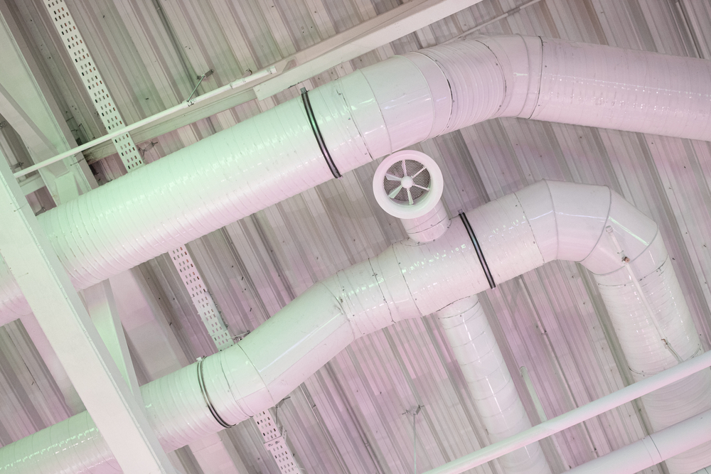 Industrial ventilation ducts painted in white, weaving through a ceiling with a modern industrial aesthetic, cast in soft pink and mint green lighting.