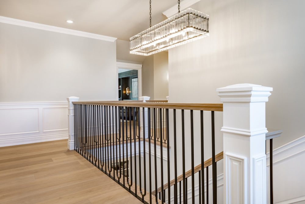 Elegant upstairs landing with a sleek iron railing, warm wood flooring, and a dazzling crystal chandelier.