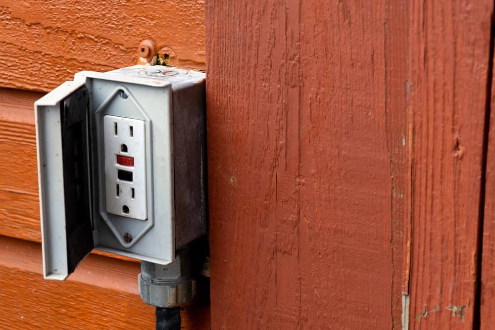 Outdoor GFCI electrical outlet mounted on a red-painted wooden wall