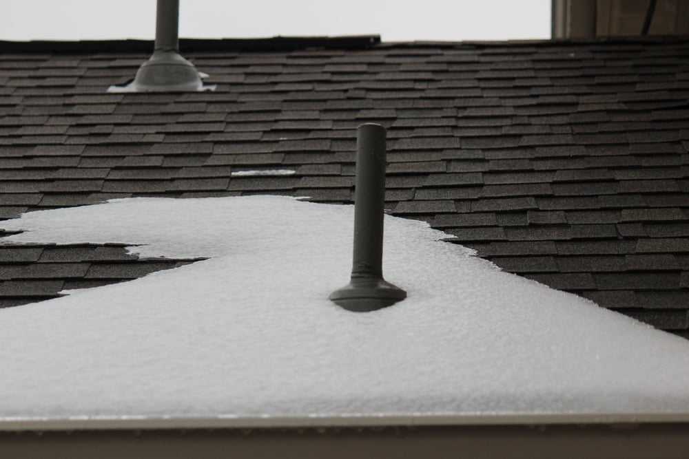Snow partially covers a rooftop, melting around a vent pipe.