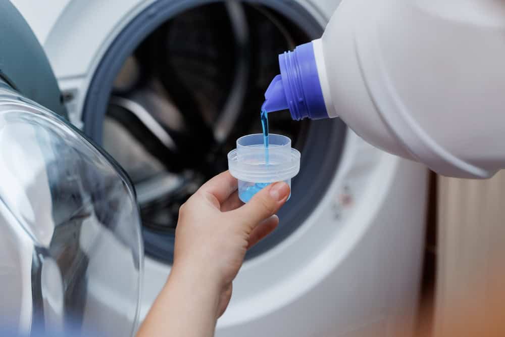Pouring liquid detergent into a measuring cup for laundry day.