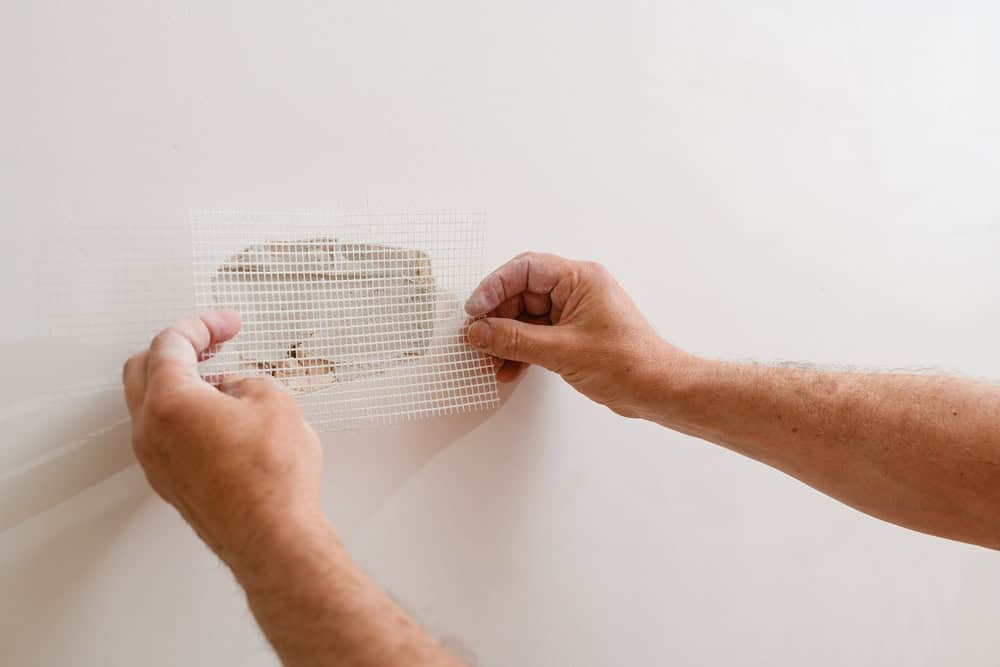 Repairing a wall with a patch of drywall mesh tape.