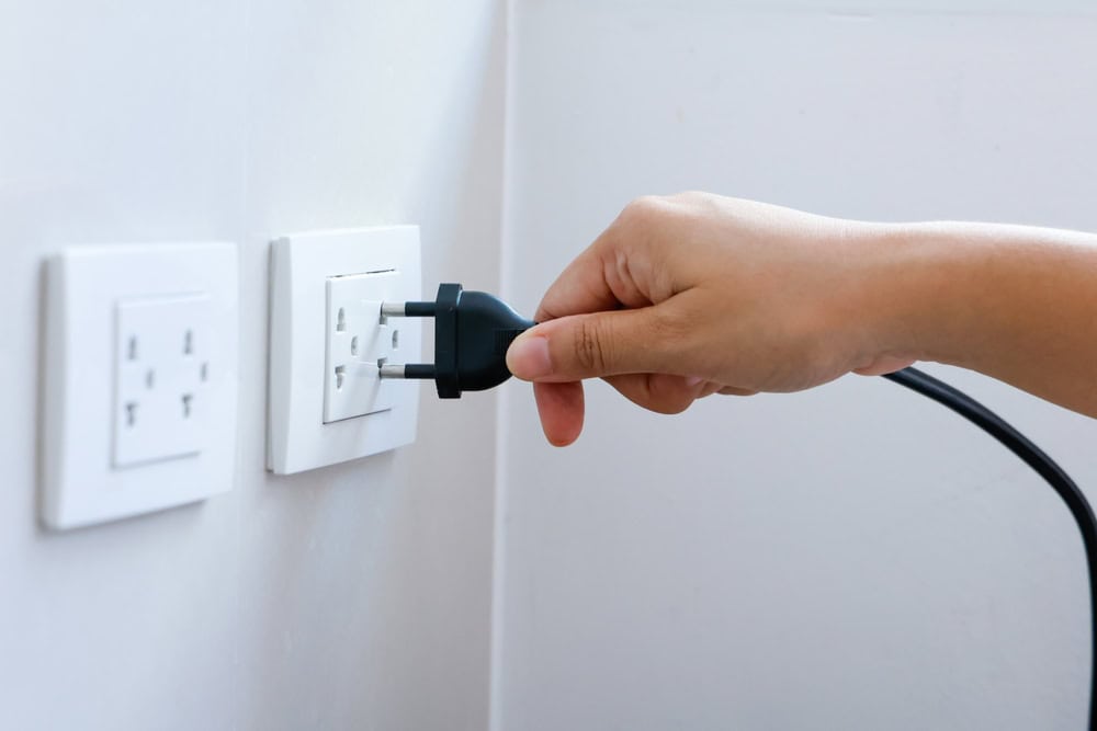Hand plugging a black electrical cord into a white wall socket