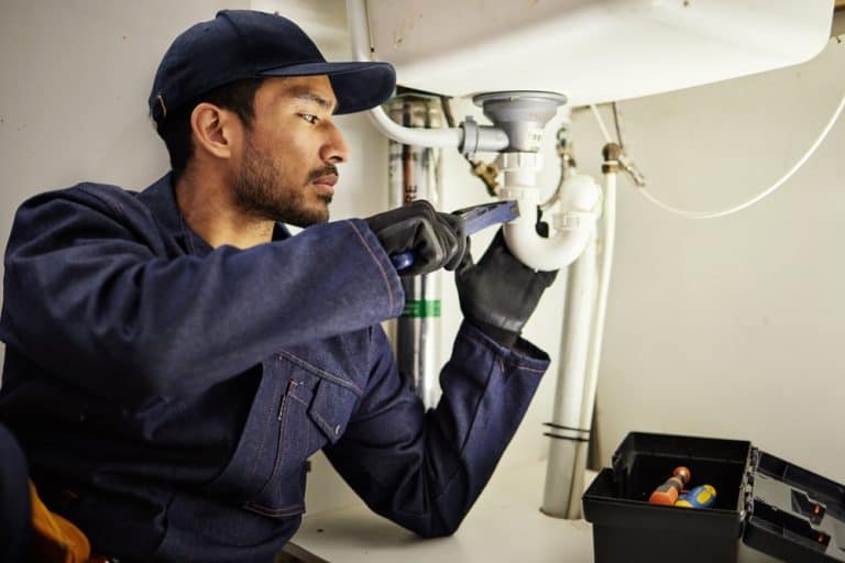 Focused plumber in uniform repairs under-sink piping.