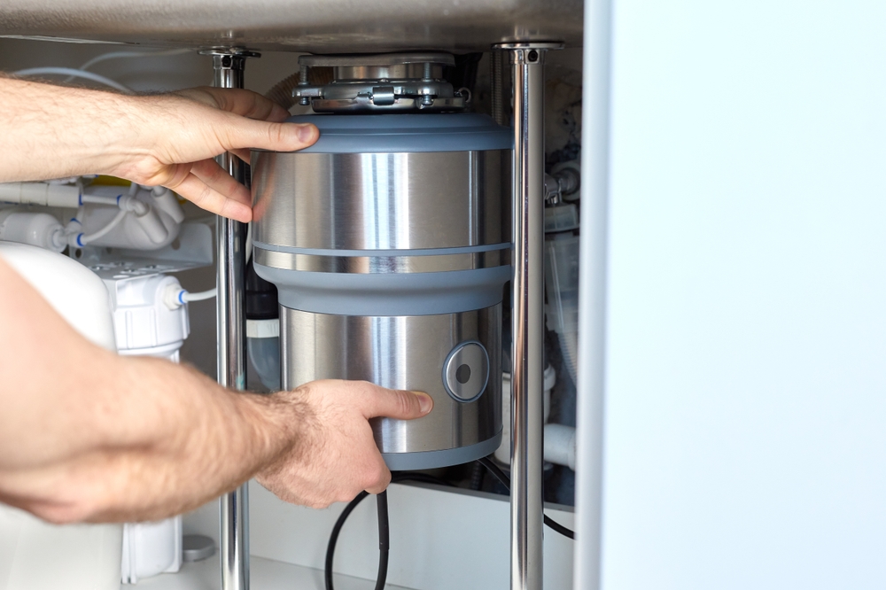 Hands servicing a garbage disposal unit mounted under a kitchen sink