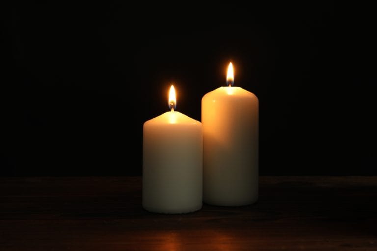Two lit candles casting a warm glow against a dark background.