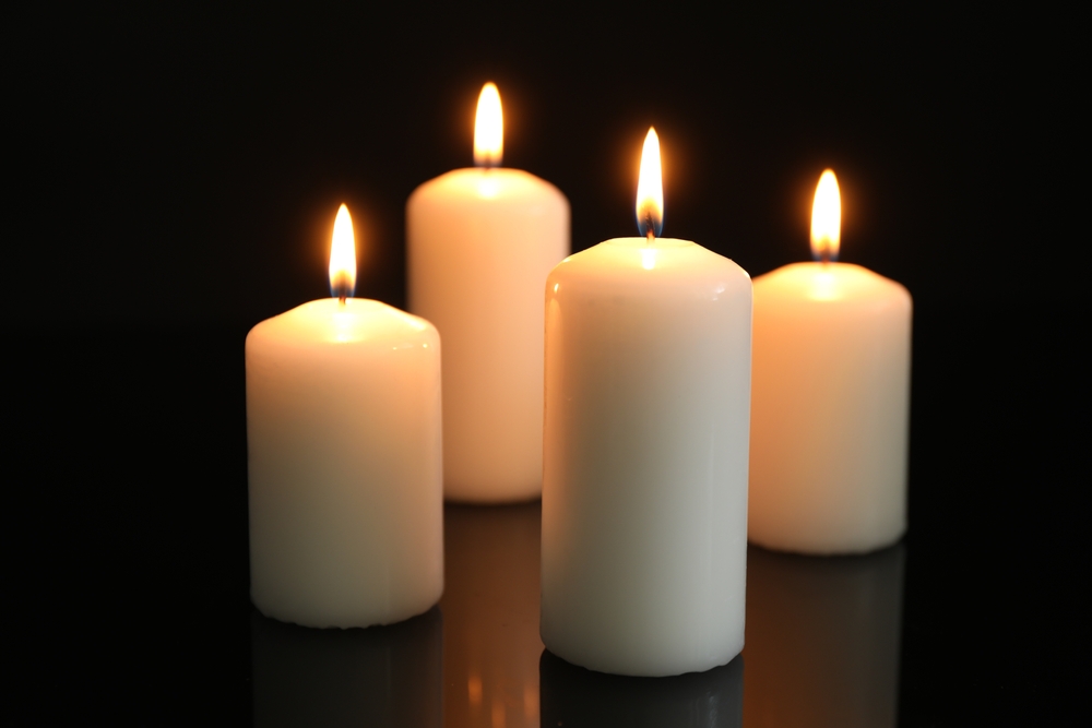 Four white pillar candles burning brightly against a dark background, casting a warm, peaceful glow