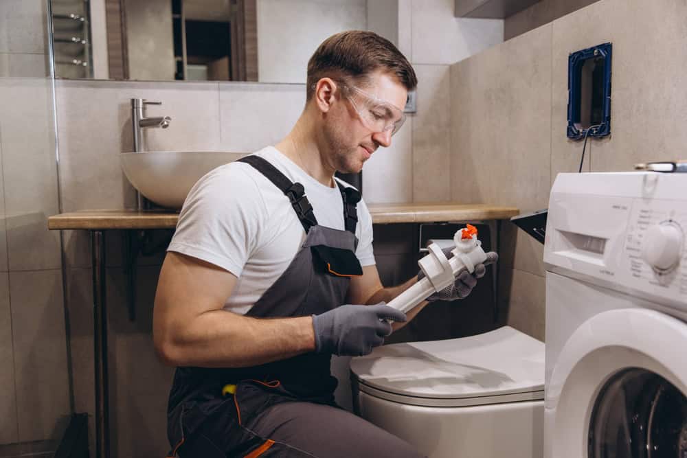 Plumber inspecting toilet fill valve in bathroom.