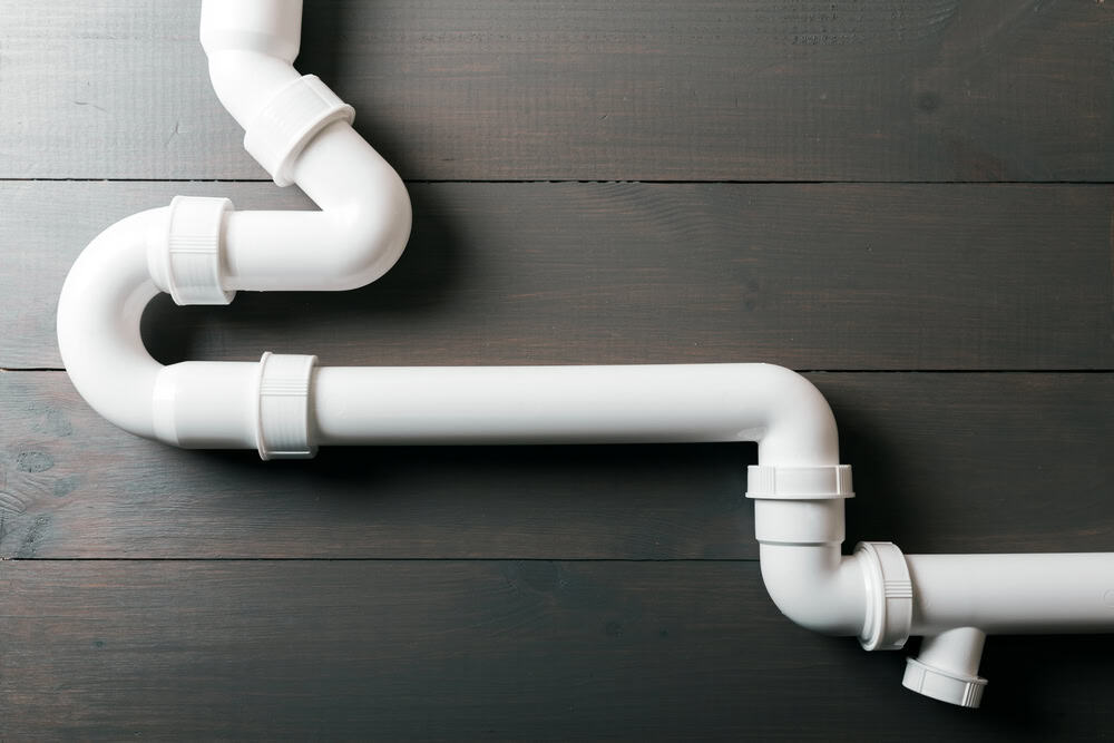 White PVC plumbing pipes arranged in a zigzag pattern over dark wooden boards.