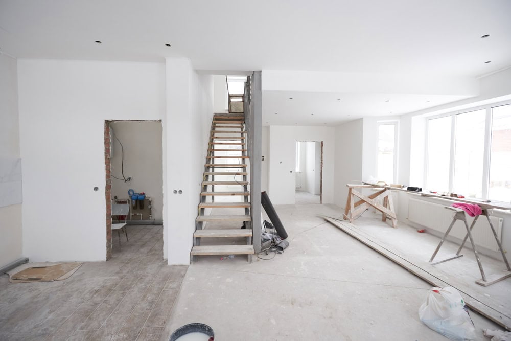 A modern home under construction with wooden stairs, large windows, and scattered building materials.