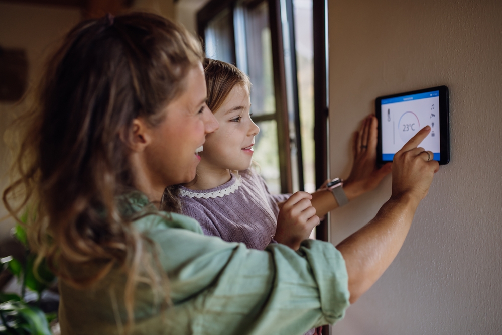 A young family adjusts their smart home thermostat together, sharing a joyful moment while managing their home's temperature at 23°C.