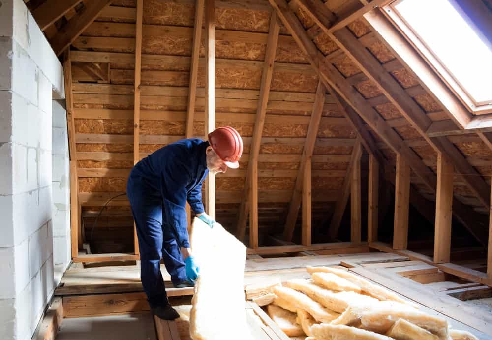 Worker installing insulation in a wooden attic to improve energy efficiency.