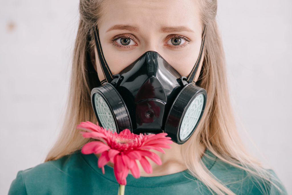 Contrast in Crisis: A bright pink gerbera daisy stands out against a black respirator mask, worn with a teal top. The striking juxtaposition highlights both protection and natural beauty in modern times.